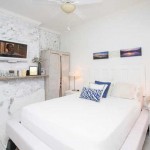 The bed in White Room, pictures hanging on wall above bed, and side table with lamp.