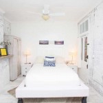 Center view of the bed in White Room with a blue stripped pillow, and side tables with lamps on each side of the bed.