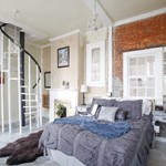 Gray comforter drapes this queen bed with the backdrop of white stained window, wood sprial staircase